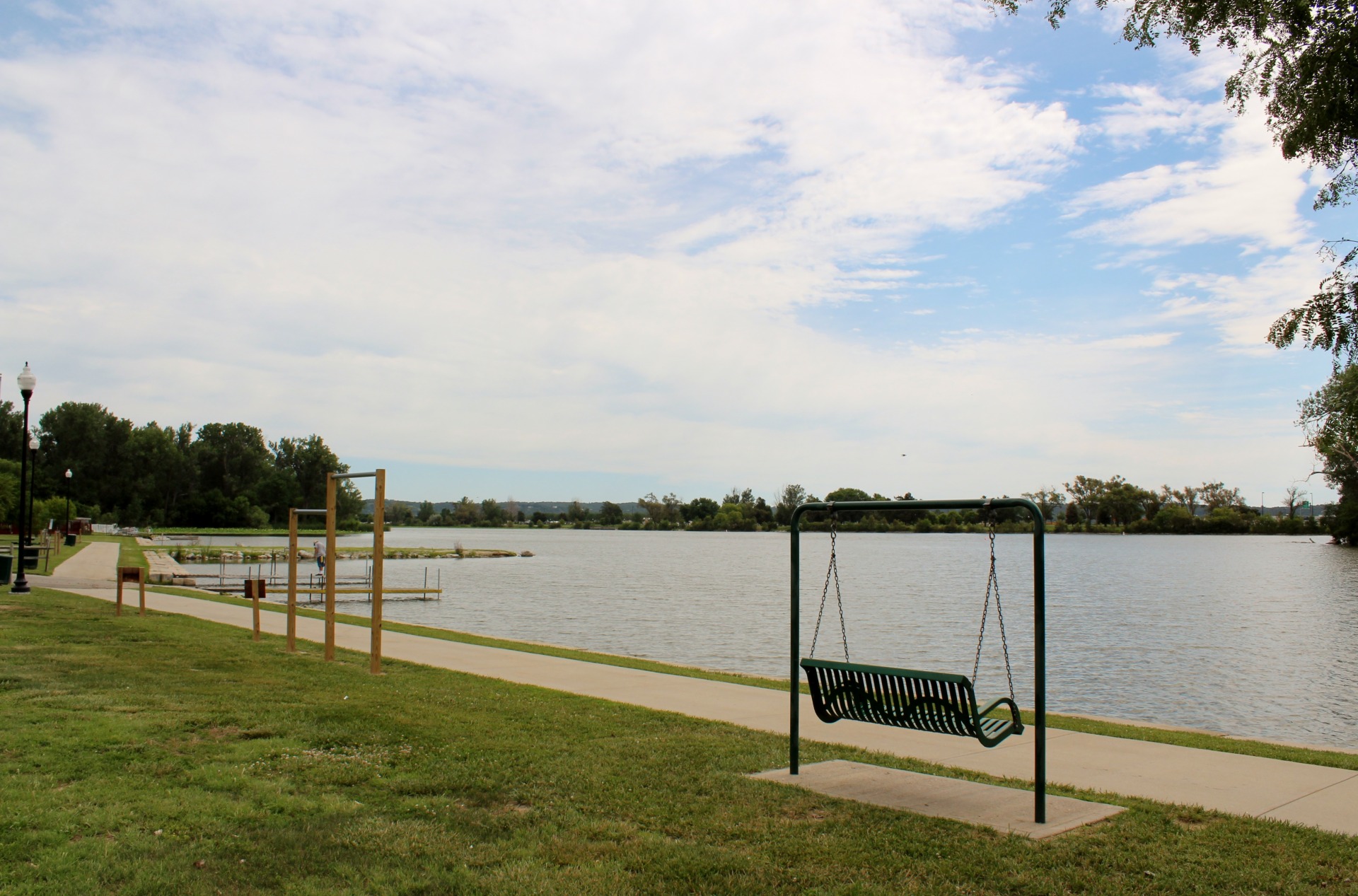 Paved trail leading around Carter Lake. Along the rail are a bench swing and pullup bars.
