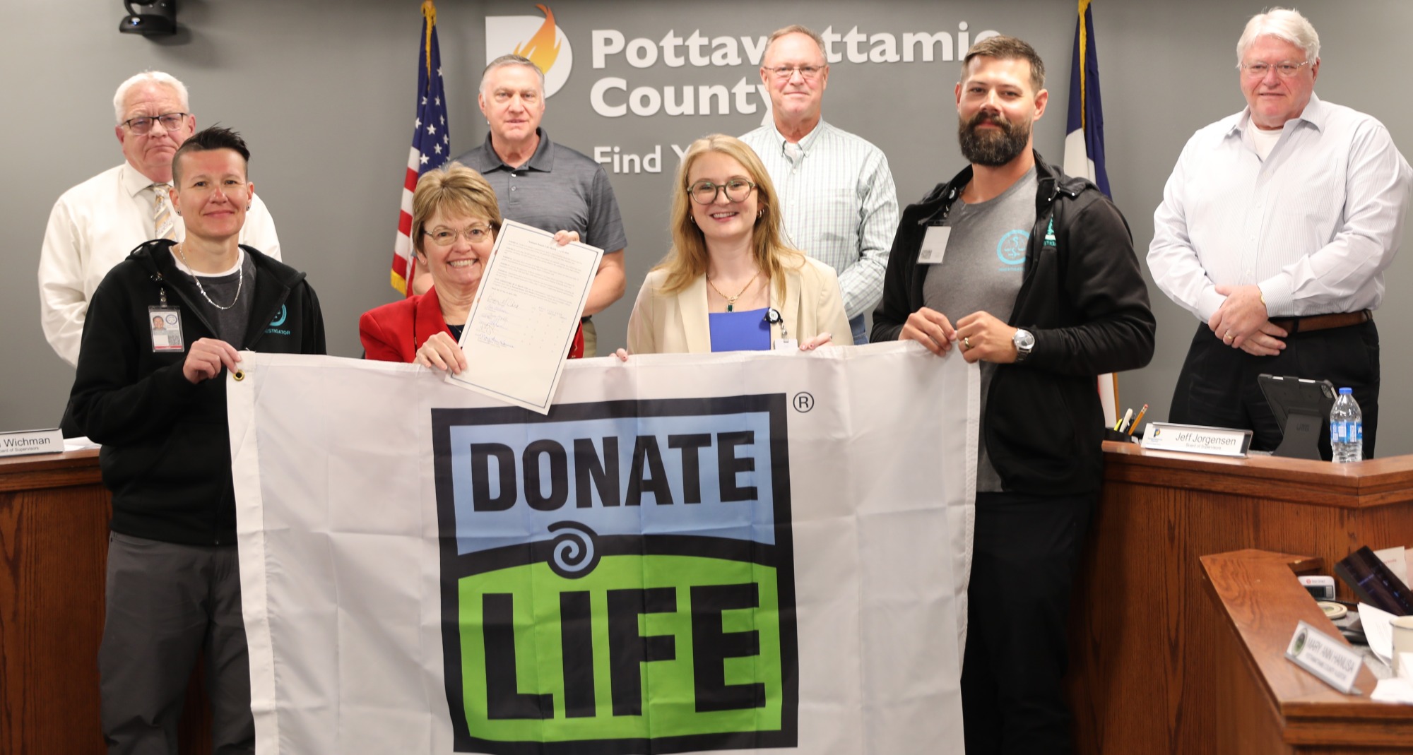 Donate Life flag being held by members of Medical Examiners Office and Iowa Donor Network and Board of Supervisors